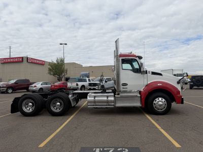 Kenworth T880 truck in a parking lot, side view showing cab with red front and chrome fuel tanks, dual rear axles, standard sleeper cab door.