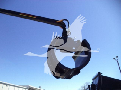 Grapple bucket attachment suspended in the air, part of a roll-off truck setup, hydraulic arm reaching to lift a metal bucket.