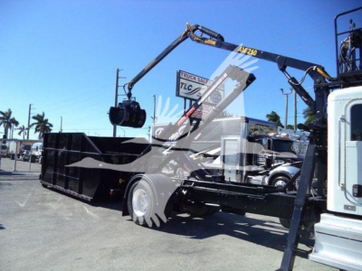 Peterbilt 337 roll-off truck in yard with hydraulic crane, bed extended, front cab visible on right, stock and VIN tags not legible.
