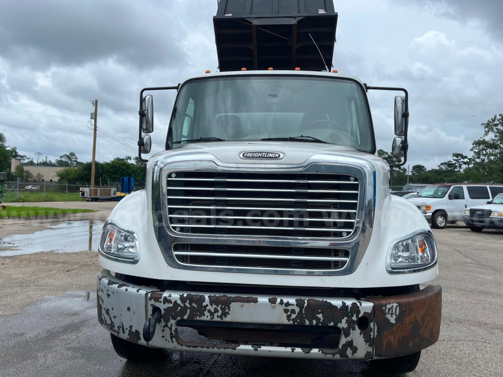 Front view of a Freightliner M2 112 dump truck showing chrome grille, headlights, windshield, and rust-speckled front bumper.