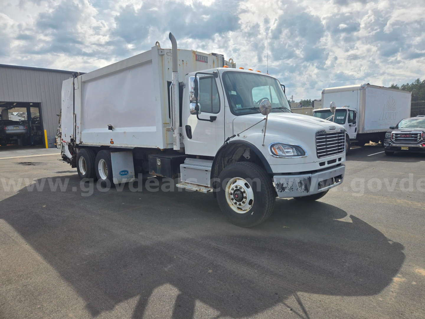 Truck cab and dump bed of a Freightliner M2 garbage truck showing side view with white cab and large dump body.