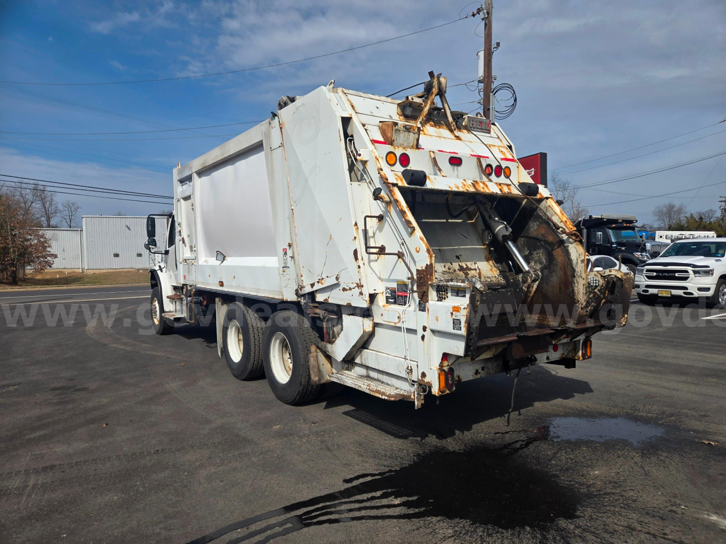 Truck rear view of a white 2020 Freightliner M2 garbage truck with dump body and rust spots, parked in lot.