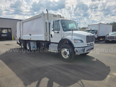 Truck cab and dump bed of a Freightliner M2 garbage truck showing side view with white cab and large dump body.