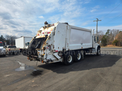 Truck chassis and rear loader of a 2020 Freightliner M2 garbage truck with white body, dumping mechanism at rear, in-use condition.