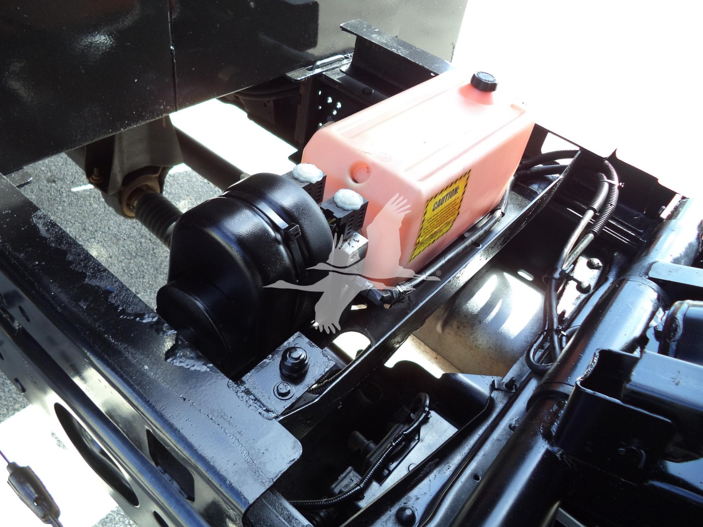 Engine bay of a 2017 Ford F450 dump truck showing a pink coolant reservoir with warning label, a black air intake housing, and surrounding metal framework.
