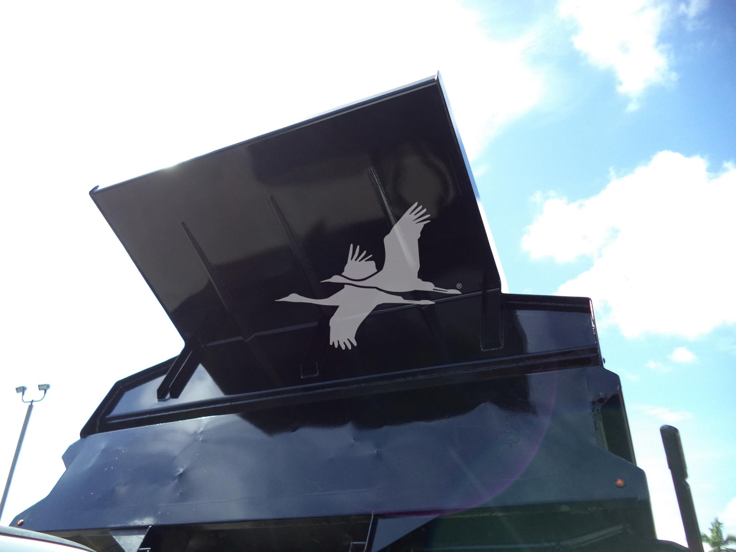 Truck dump body with raised tailgate and open bed lid showing Ford logo silhouette on the side.
