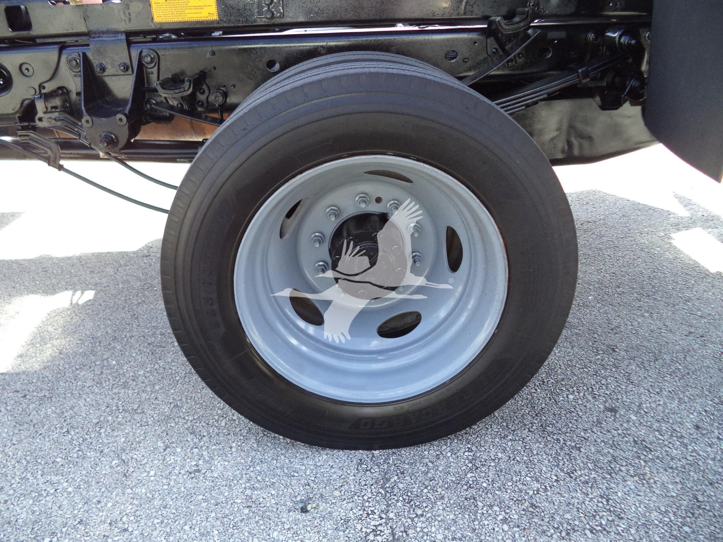Wheel and front axle area of a 2017 Ford F450 XL dump truck showing a black tire mounted on a light gray steel wheel with exposed suspension components and chassis.