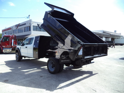 Ford F-450 dump truck with tilt bed raised, white cab and black dump body, side view showing rear wheels and hydraulic mechanism.