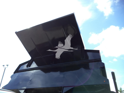 Truck dump body with raised tailgate and open bed lid showing Ford logo silhouette on the side.