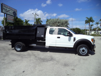 Ford F-450 dump truck side view showing white cab and black dump bed with TLC sign in background.