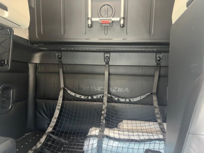 Truck cab interior showing sleeper area with cargo net across back wall and storage shelf above.
