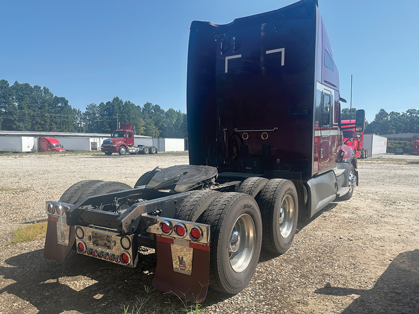 Kenworth T680 tractor rear three-quarter view showing dual rear axles, fifth wheel, and mud flaps with Kansas-style paint; visible rear lights and reflective plates.
