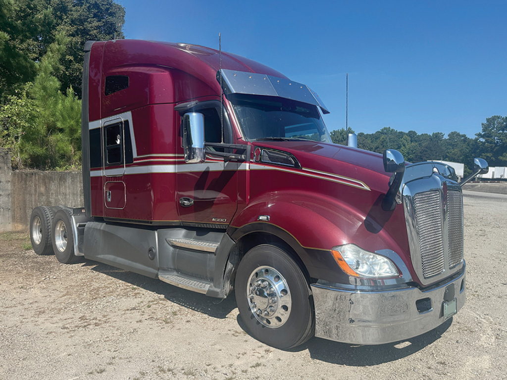 Kenworth T680 dark red/ maroon sleeper tractor truck, side view, chrome front bumper, dual rear axles, chrome wheels, aluminum fuel tanks, daytime outdoor lot.