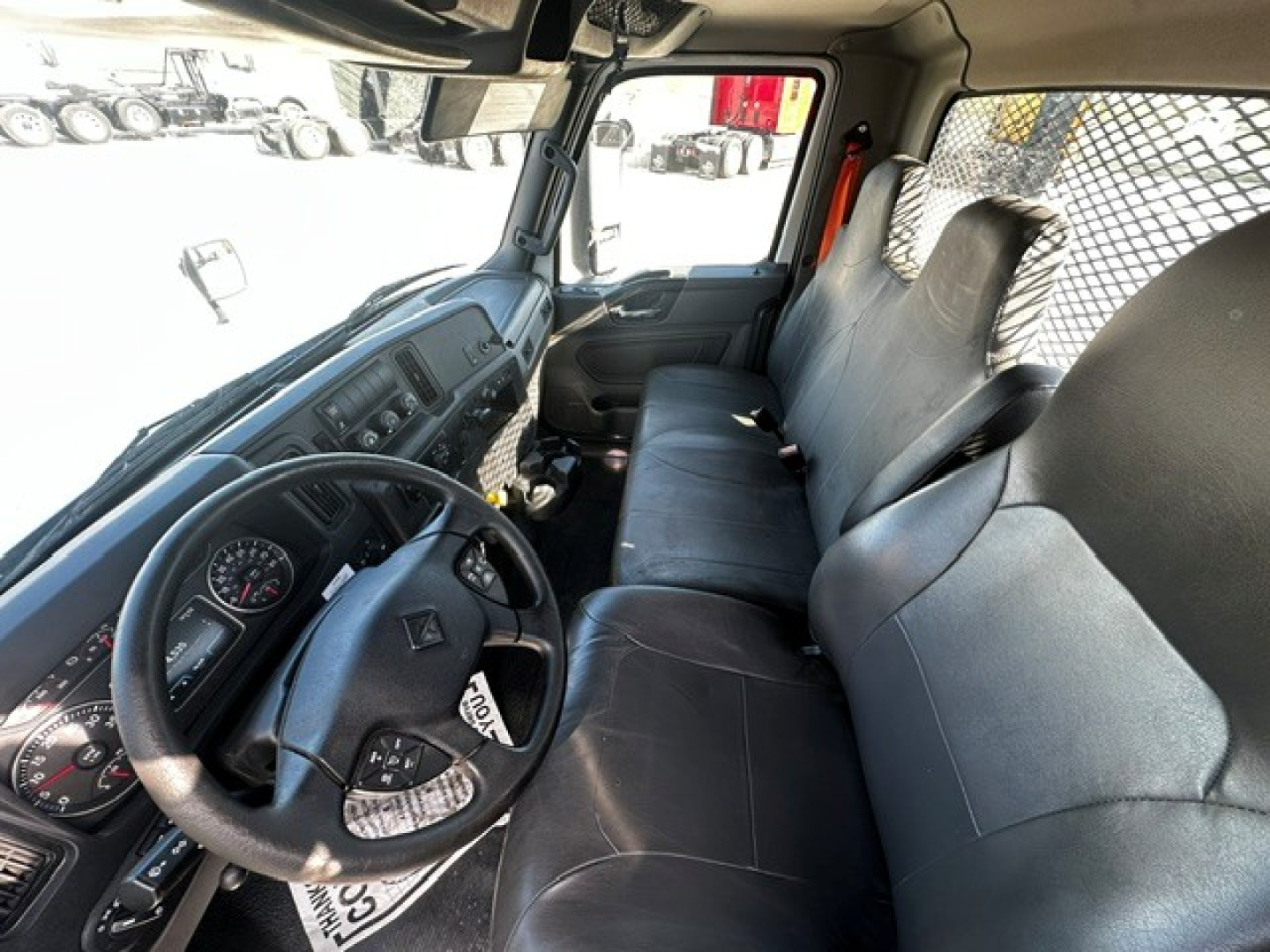 Truck cab interior of a 2020 International MV607 showing dashboard, steering wheel, driver seat, and bench seat with mesh partition in background.