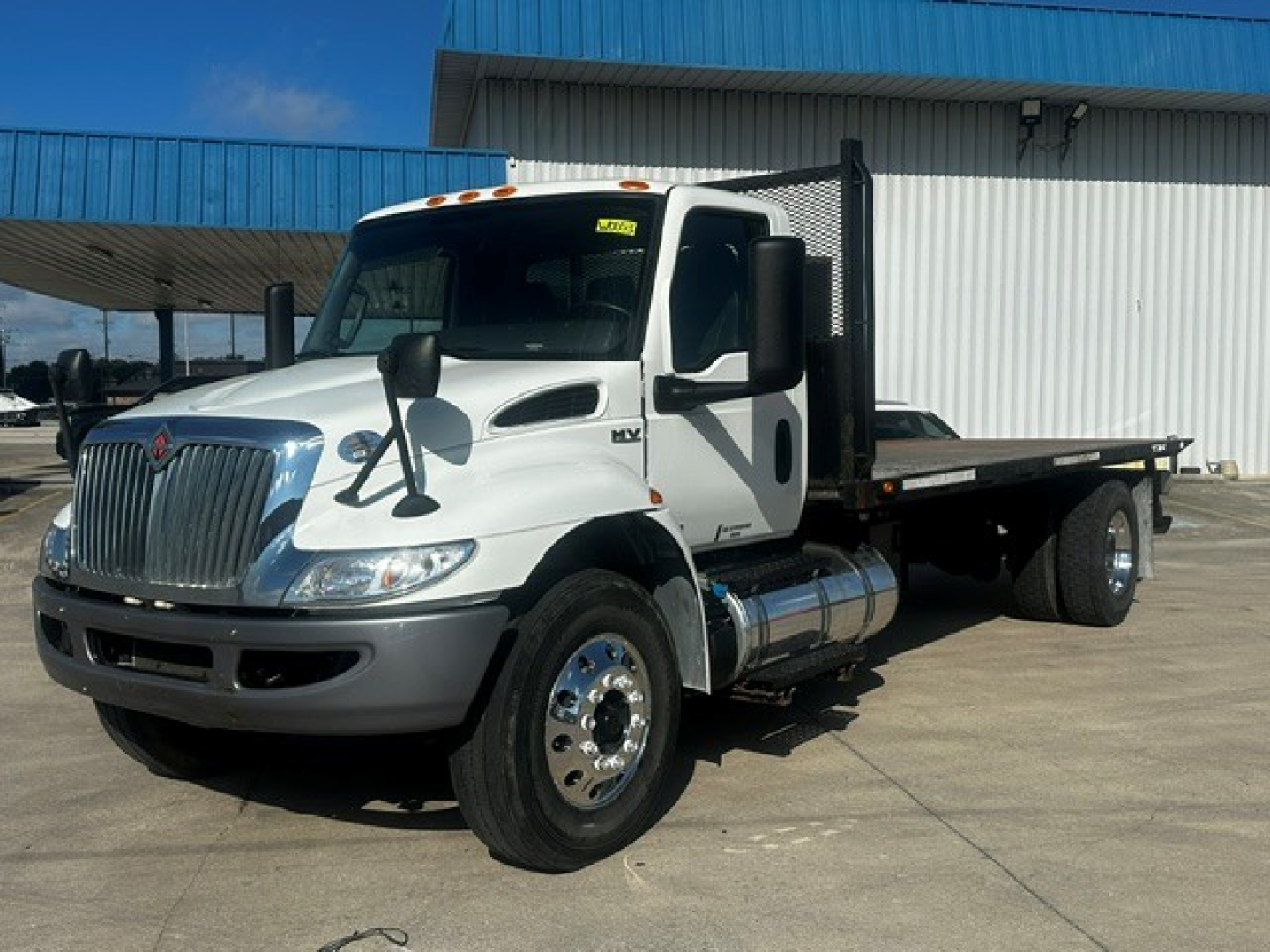 International MV Series tow truck side view showing flatbed and dual rear wheels, white cab with black mirrors and chrome fuel tanks.