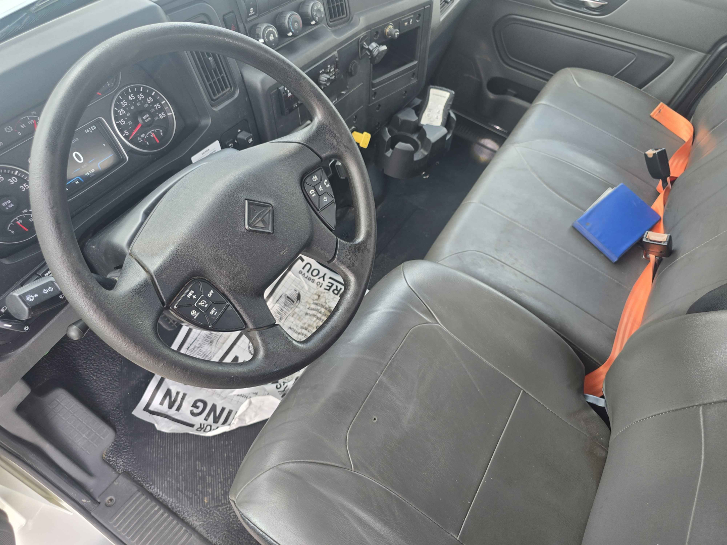 Interior of 2020 International MV607 cab showing steering wheel and front bench seat with orange seat belts.