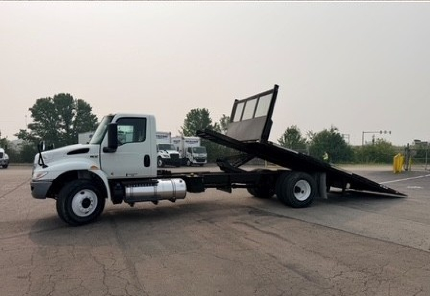 White International MV Series tow truck with a tilt bed, side view showing wheel, cab, and hydraulic tilt bed raised.