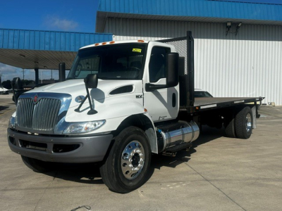 International MV Series tow truck side view showing flatbed and dual rear wheels, white cab with black mirrors and chrome fuel tanks.