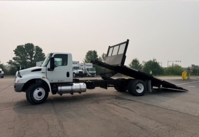White International MV Series tow truck with a tilt bed, side view showing wheel, cab, and hydraulic tilt bed raised.