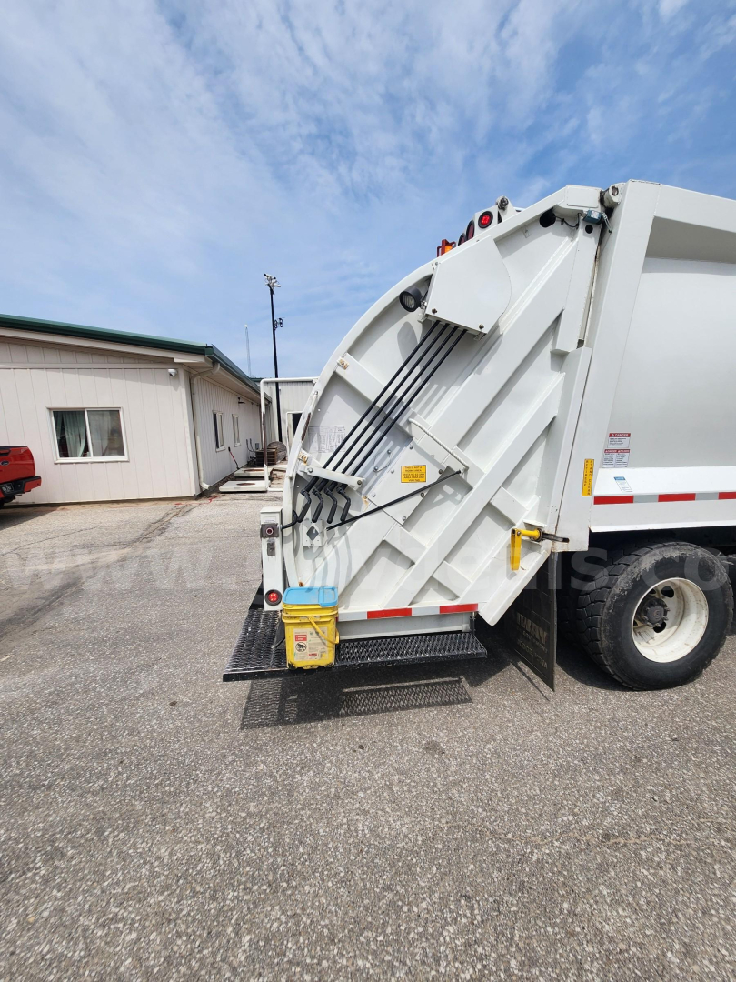 Dump truck rear showing tailgate and hydraulic hoist with yellow caution label and white body.