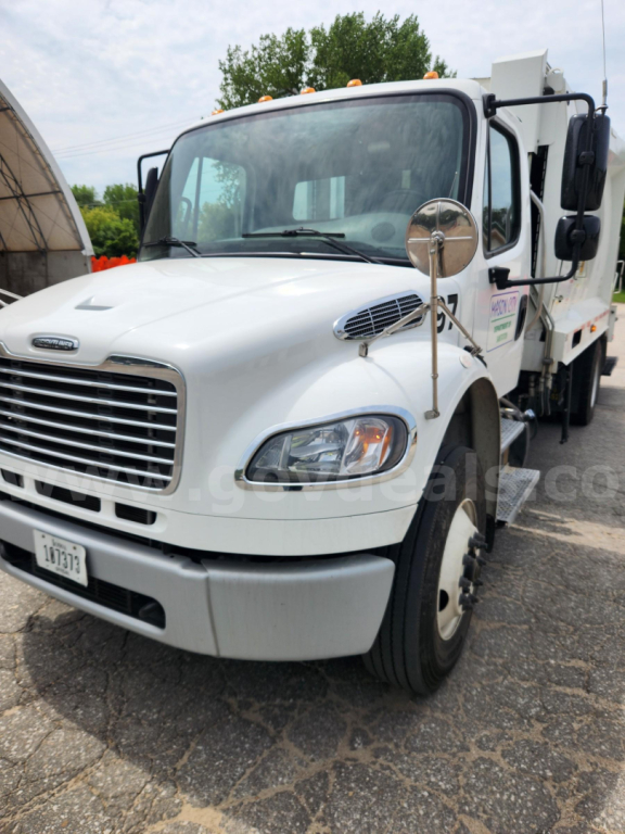 Truck cab of a 2021 Freightliner M2 106 viewed from front-right, white exterior, garbage truck body, side mirror, headlights visible.
