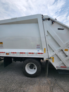 Freightliner M2 106 dump truck side view showing rear wheel and dump body with safety decals and latch hardware.