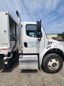 Freightliner M2 106 side cab view showing garbage truck body and Mason City Department of Sanitation logo on door, number 97 on fender, step/side stairs.