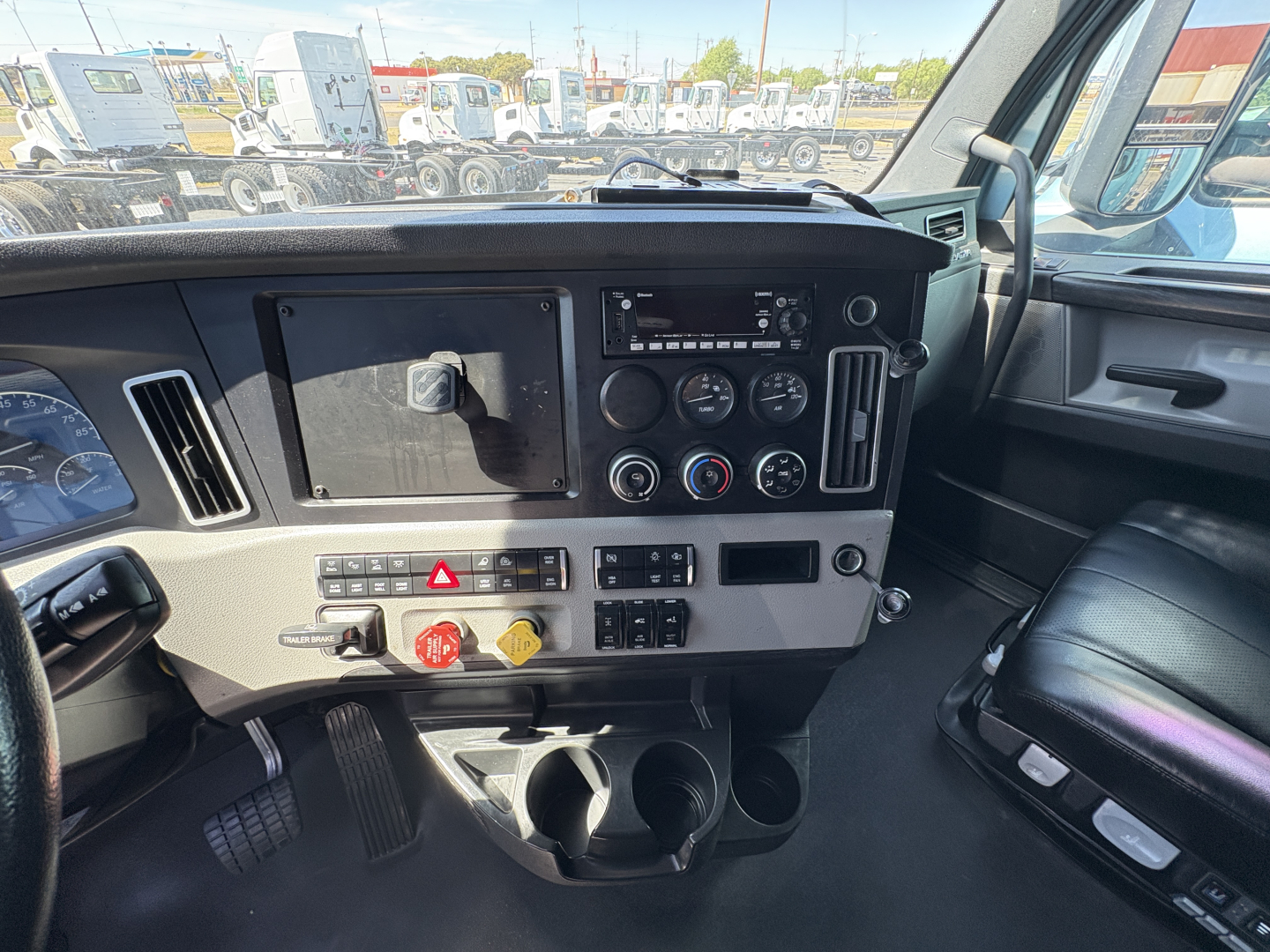 Truck cab dashboard interior showing steering column, radio, climate controls, warning lights, cup holders, and storage pockets.