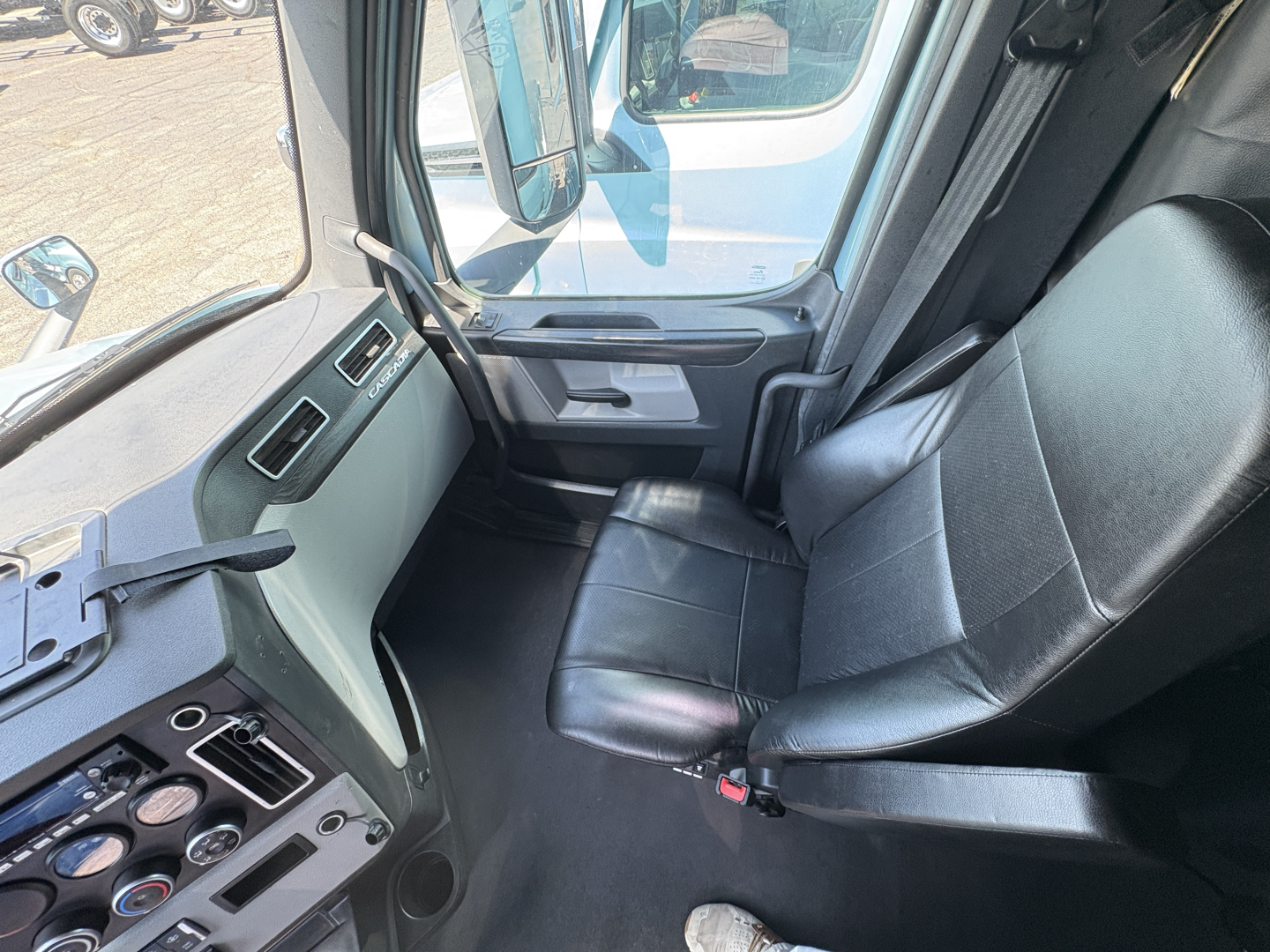 Cab interior of a Freightliner Cascadia 126 truck showing black leather seat, driver-side door area, dashboard gauges and controls.