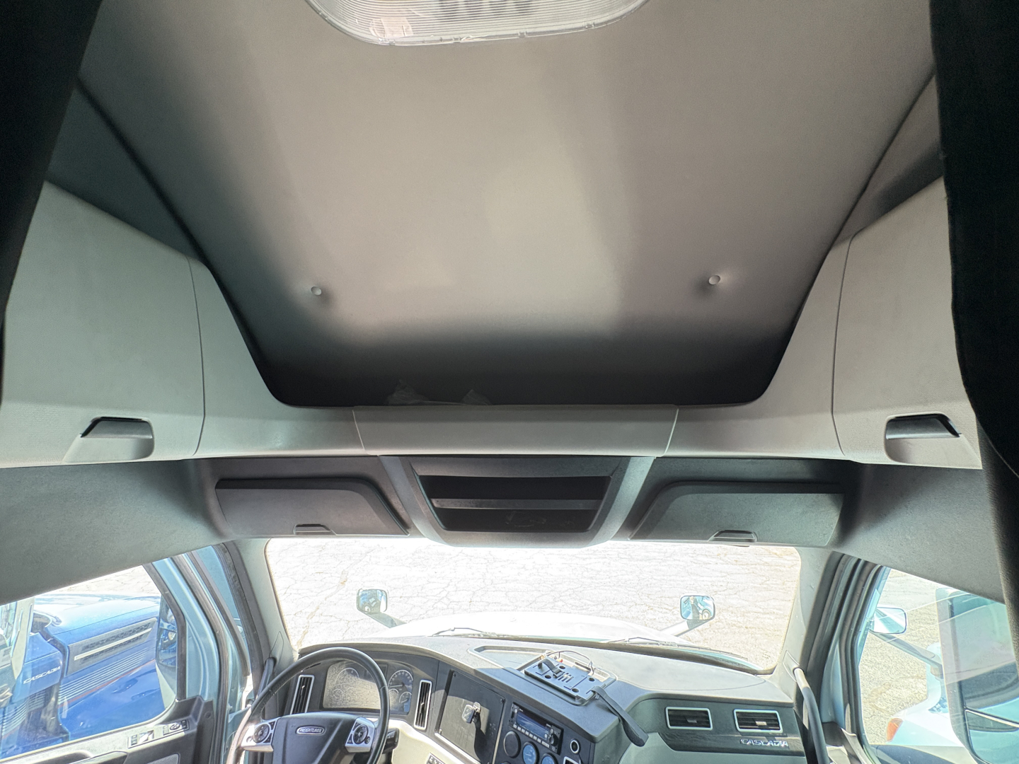Cab interior of a 2023 Freightliner Cascadia 126 tractor showing dashboard, steering wheel, overhead console, and sun visor; heater/AC vents visible.