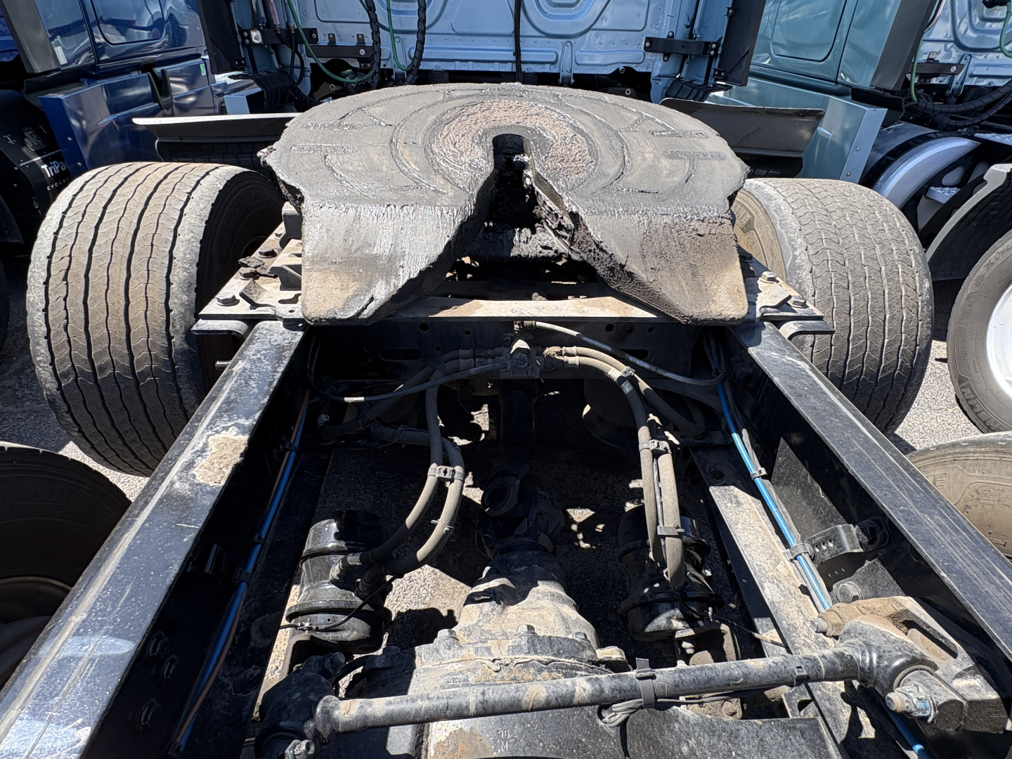 Truck chassis view showing fifth wheel, frame rails, air lines, and suspension components from a Freightliner Cascadia 126 cab with exposed drivetrain area.