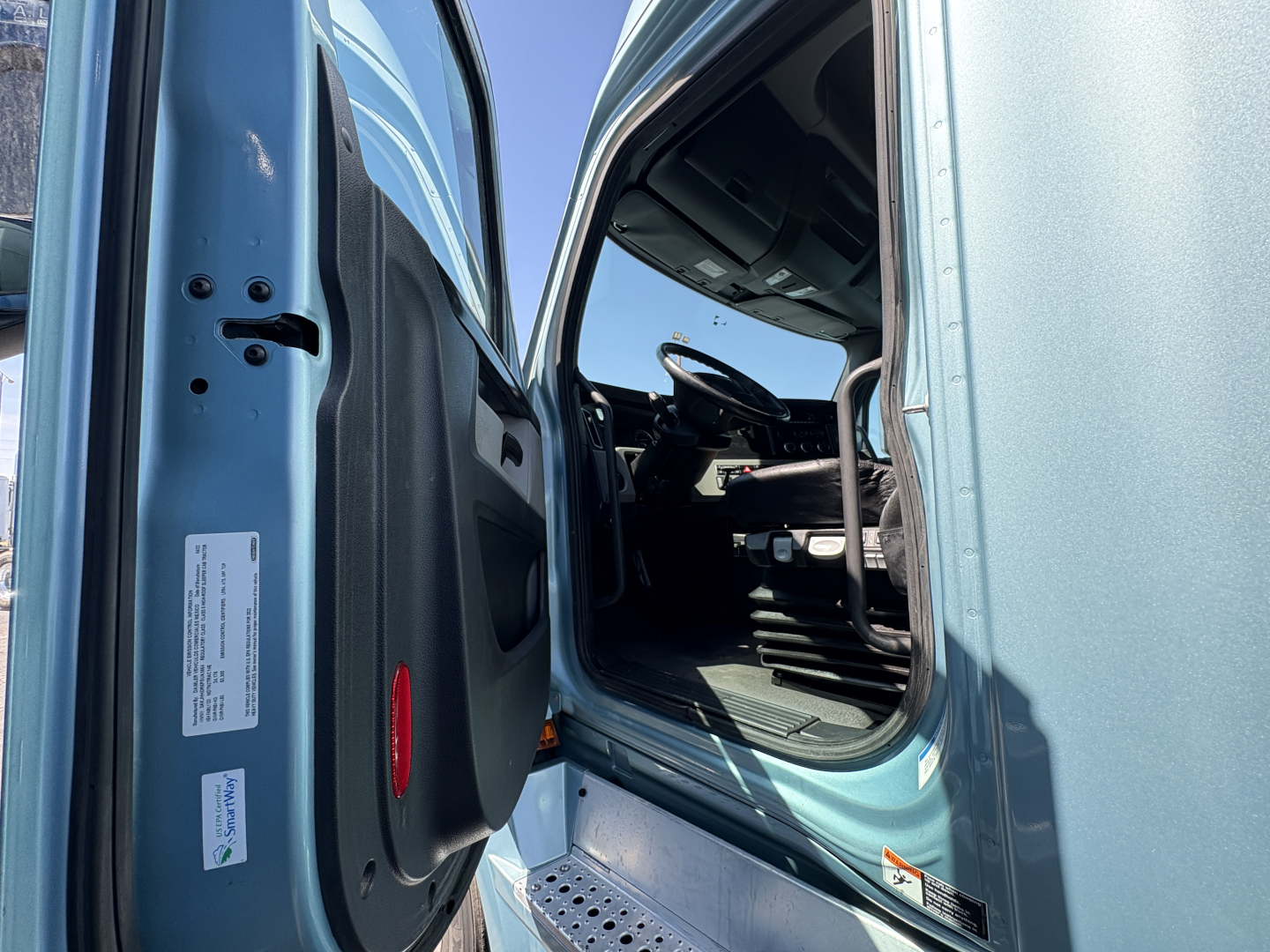 Cab interior of a Freightliner Cascadia 126 truck with door open, steering wheel, driver seat, and dashboard visible.