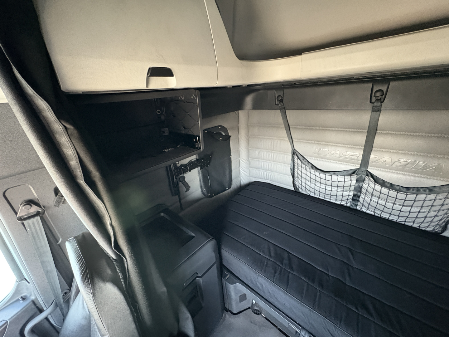 Tractor-trailer cab interior of a 2023 Freightliner Cascadia 126 sleeper showing bunk area with black cover, storage nets, and side panels.