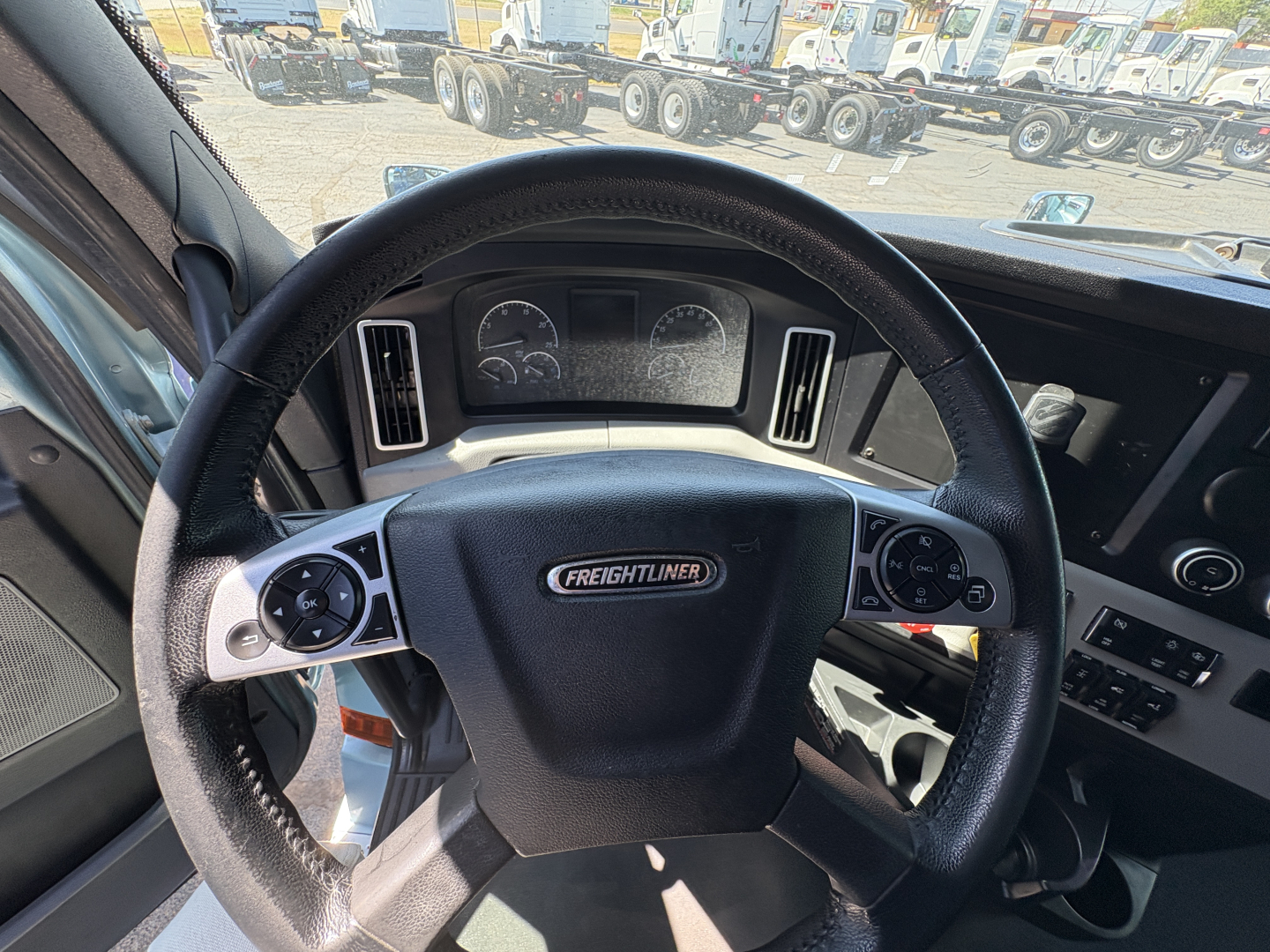 Truck steering wheel in cab with Freightliner logo, dashboard gauges, and controls visible.