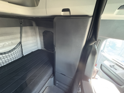 Cab interior of a Freightliner Cascadia 126 sleeper showing a bunk bed area with storage cabinet and window, detailed upholstery and a small net pocket.