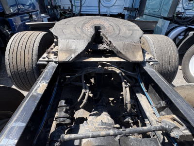 Truck chassis view showing fifth wheel, frame rails, air lines, and suspension components from a Freightliner Cascadia 126 cab with exposed drivetrain area.