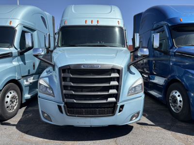 Truck front view: light blue 2023 Freightliner Cascadia 126 conventional sleeper in a dealership lot, showing grille, headlights, and side mirrors.