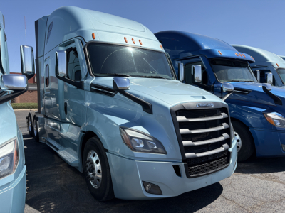 Truck cab showing Freightliner Cascadia 126 with light blue exterior and chrome grille. From left to right: light blue truck in foreground, blue trucks in background.