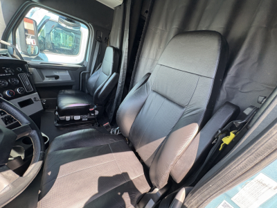 Cab interior of a Freightliner Cascadia 126 truck showing driver and passenger seats, partition curtain, and dashboard from the open door.