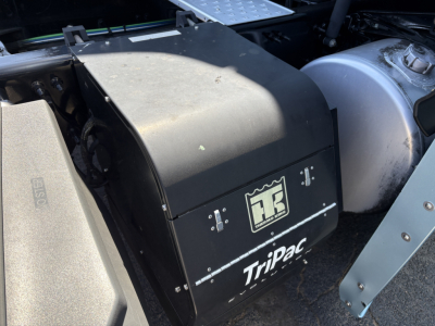TriPac auxiliary battery box mounted behind cab on Freightliner Cascadia 126 engine bay view showing TriPac label and black enclosure.