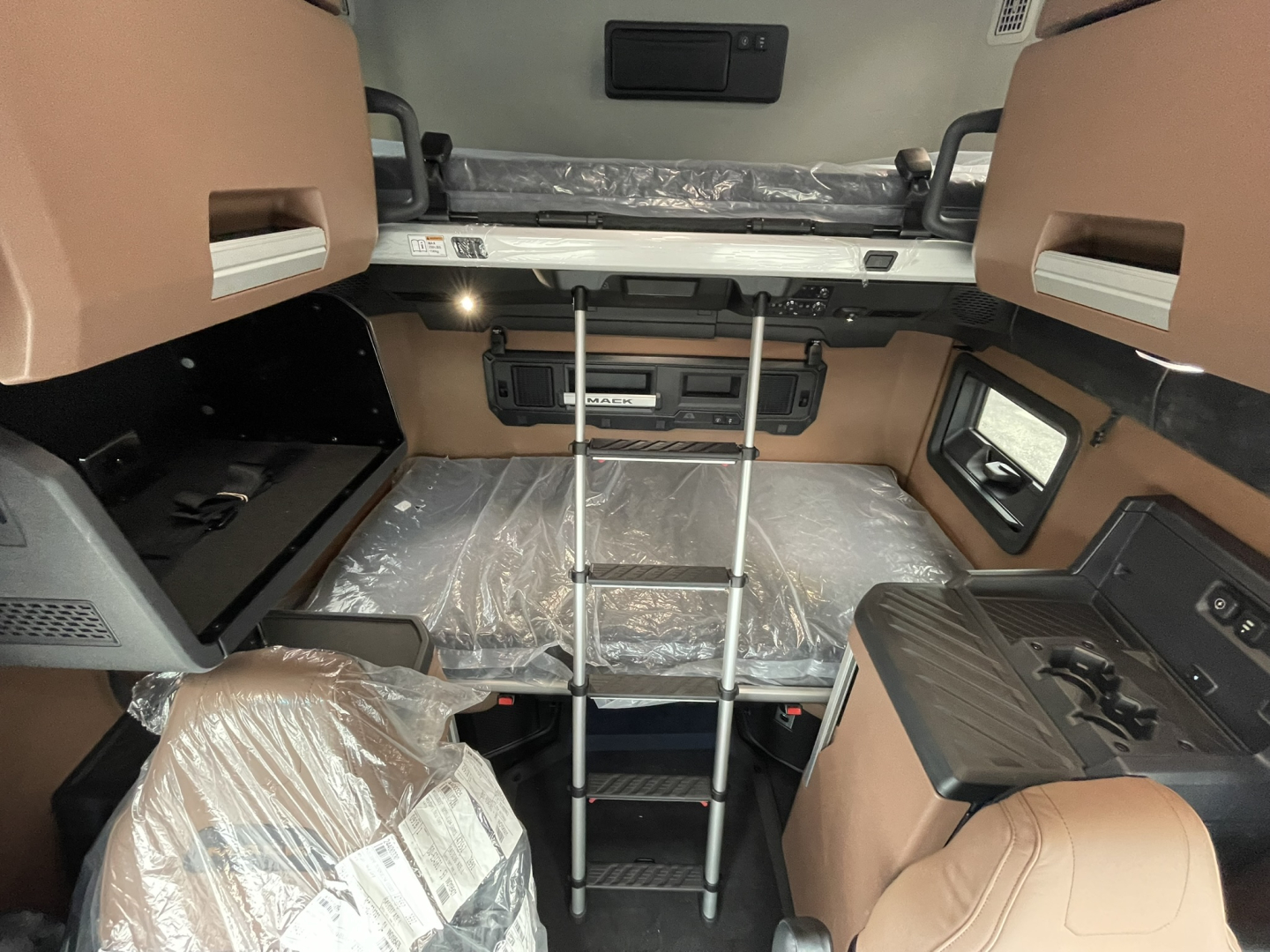 Truck cab interior showing bunk bed area with ladder, storage cabinets, and wrapped seating; brown panels and black fixtures visible.