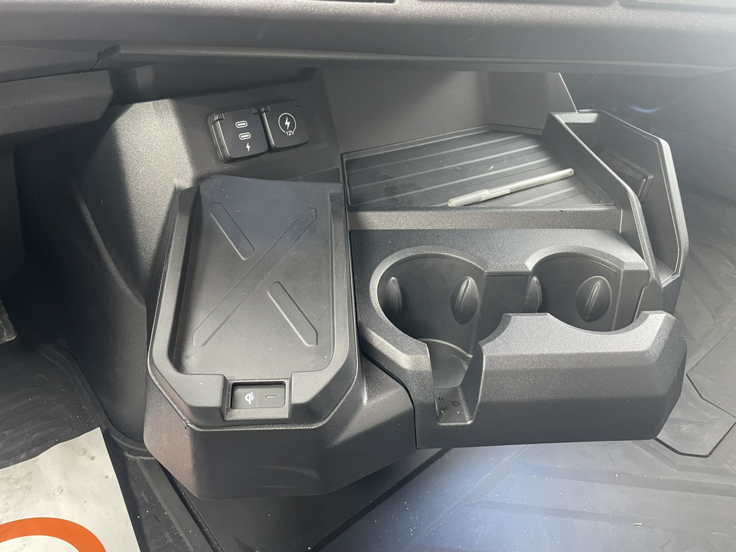 Truck interior center console area showing cup holders and small storage pockets in a Mack PR64T76H cab, with two circular cup slots and a raised lid section.