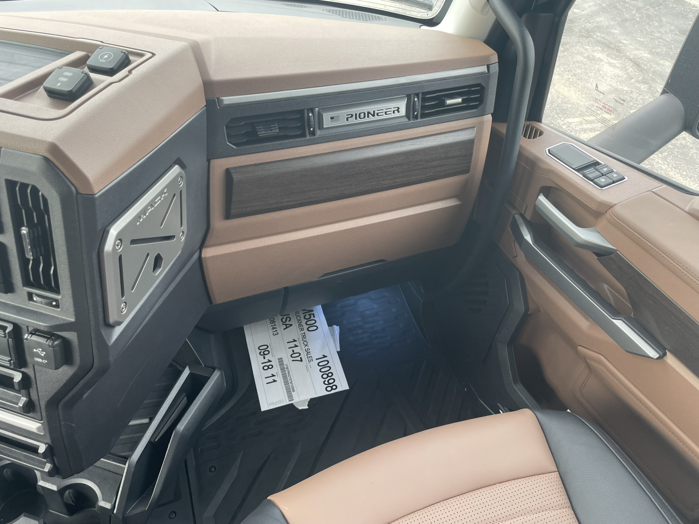 Cab interior of a Mack PR64T76H truck showing tan and brown dashboard, Pioneer radio grille, door panel, and dashboard trim with stock papers on the floor.