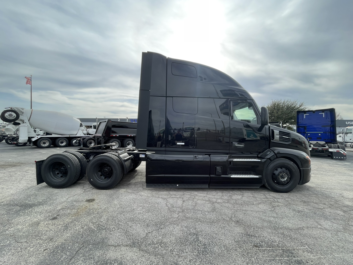 Back side view of a black Mack PR64T76H conventional sleeper tractor in a parking lot.