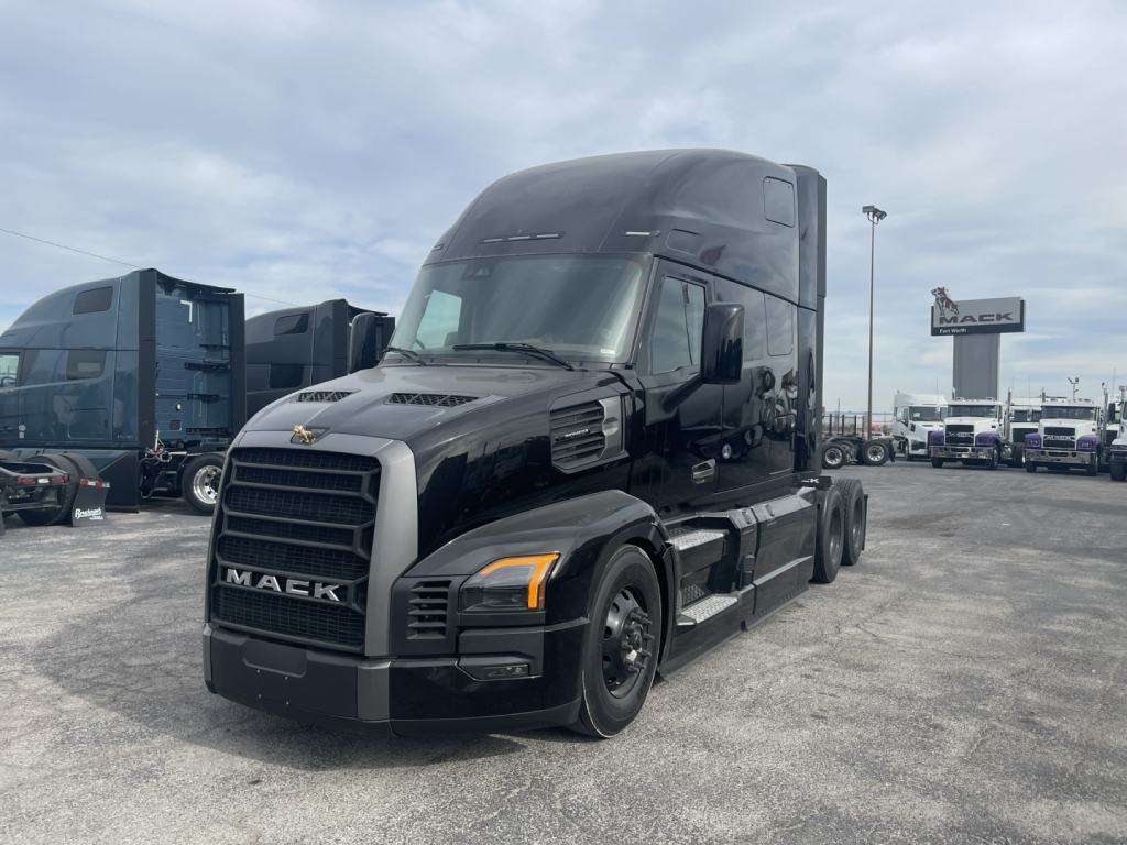 Mack PR64T76H tractor cab in a truck lot, black exterior, daytime, front left view, with chrome grille and large sleeper cab.