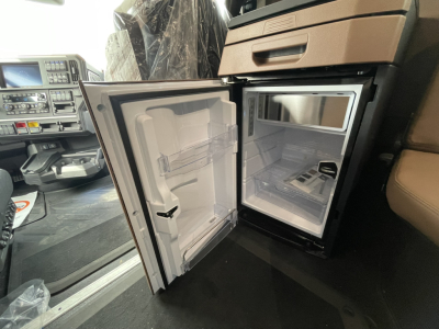 Open galley fridge in a 2026 Mack PR64T76H truck cab showing compact refrigerator with empty shelves and freezer compartment.