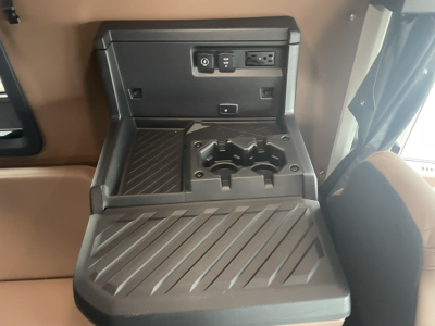 Cab interior center console in a Mack PR64T76H showing power outlet, USB, and cupholders with a ribbed fold-out tray.