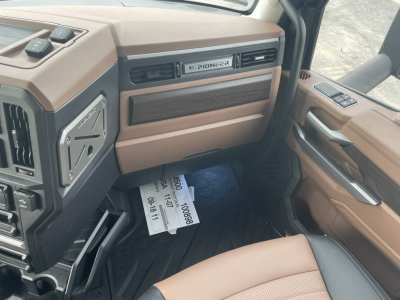 Cab interior of a Mack PR64T76H truck showing tan and brown dashboard, Pioneer radio grille, door panel, and dashboard trim with stock papers on the floor.