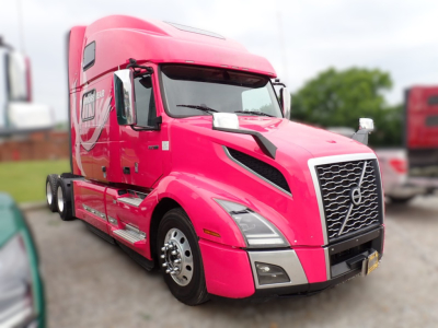 Volvo VNL cab/front view with bright pink paint, chrome grille, large side mirrors, and sleeper cab. Shows Volvo emblem on grille and headlights.