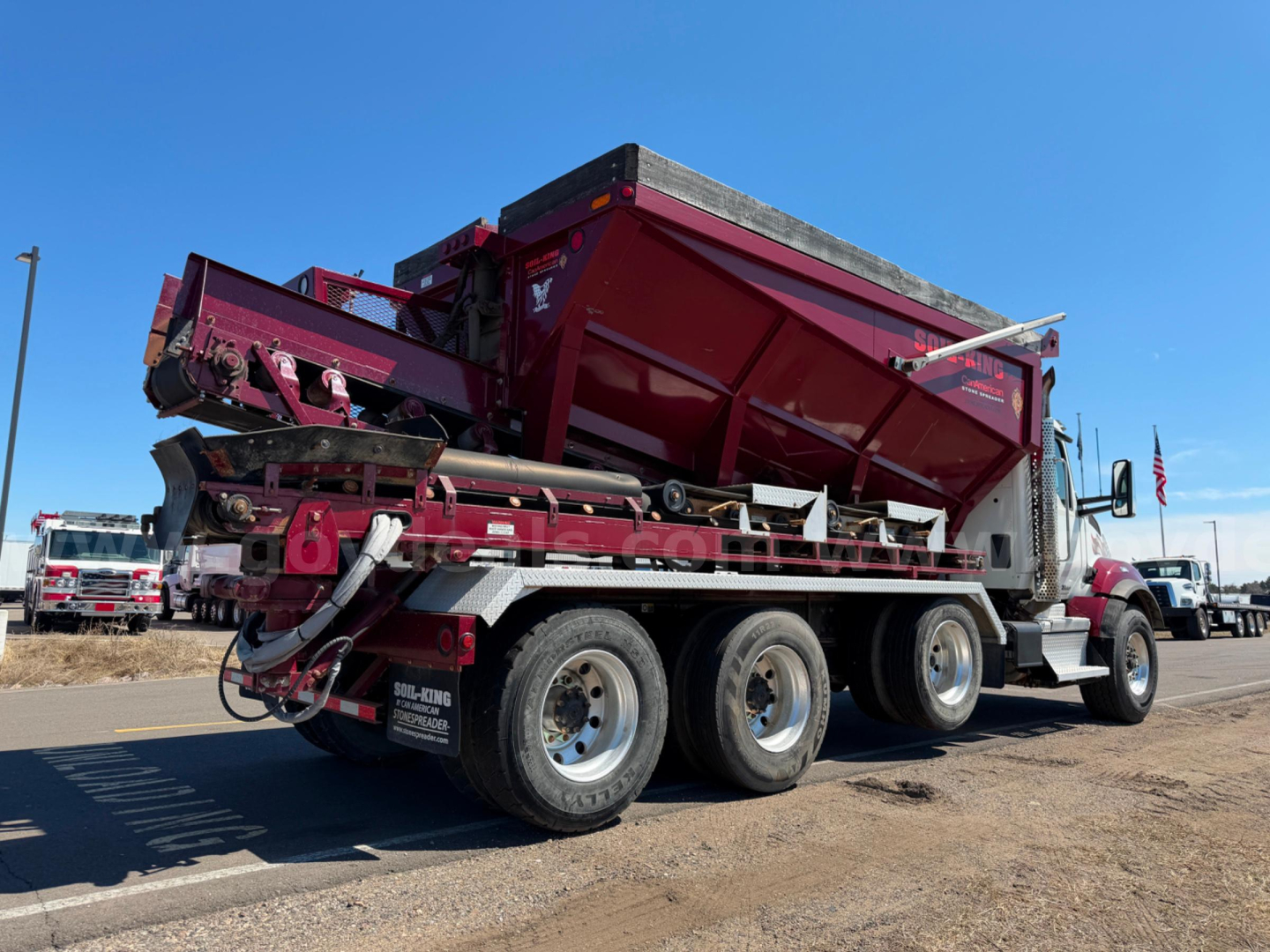 Kenworth T880 dump truck rear/side view showing six wheels, red dump bed, and attached transfer equipment.